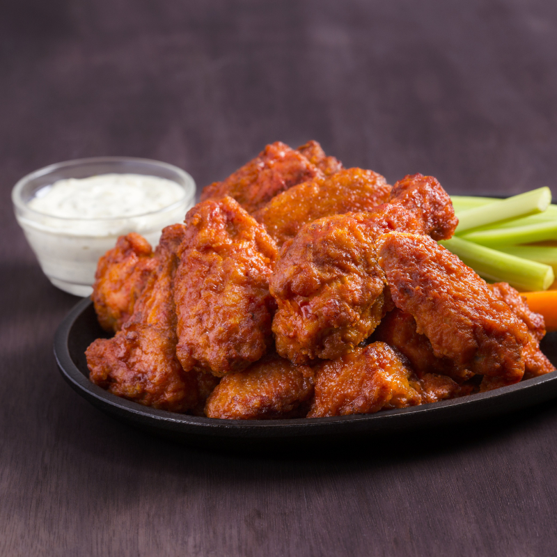 Platter of spicy buffalo chicken wings with celery sticks and a small bowl of ranch dressing on a dark wooden table.