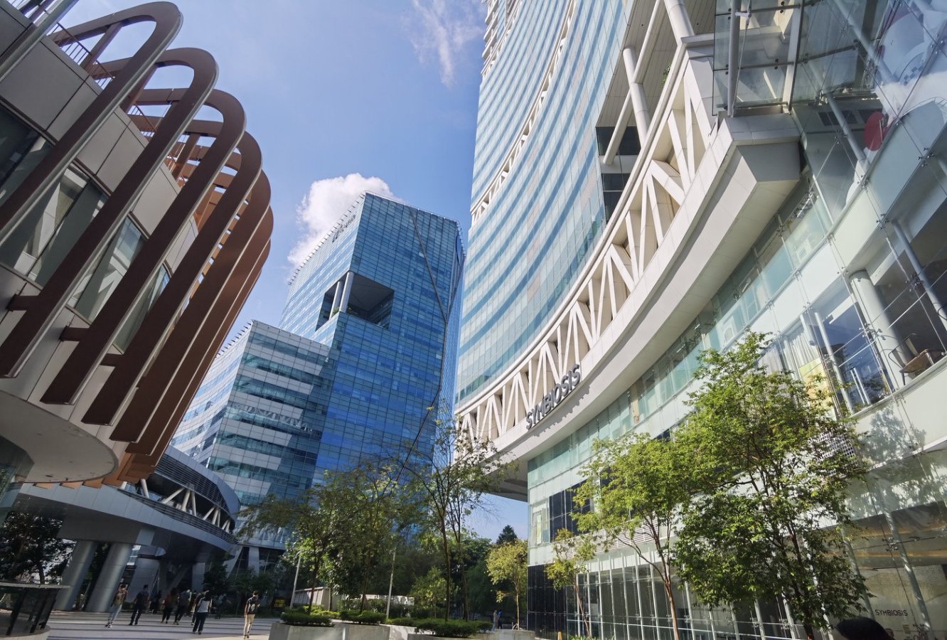 Modern skyscrapers with glass facades and trees in an urban setting, featuring a curved building and clear blue sky.