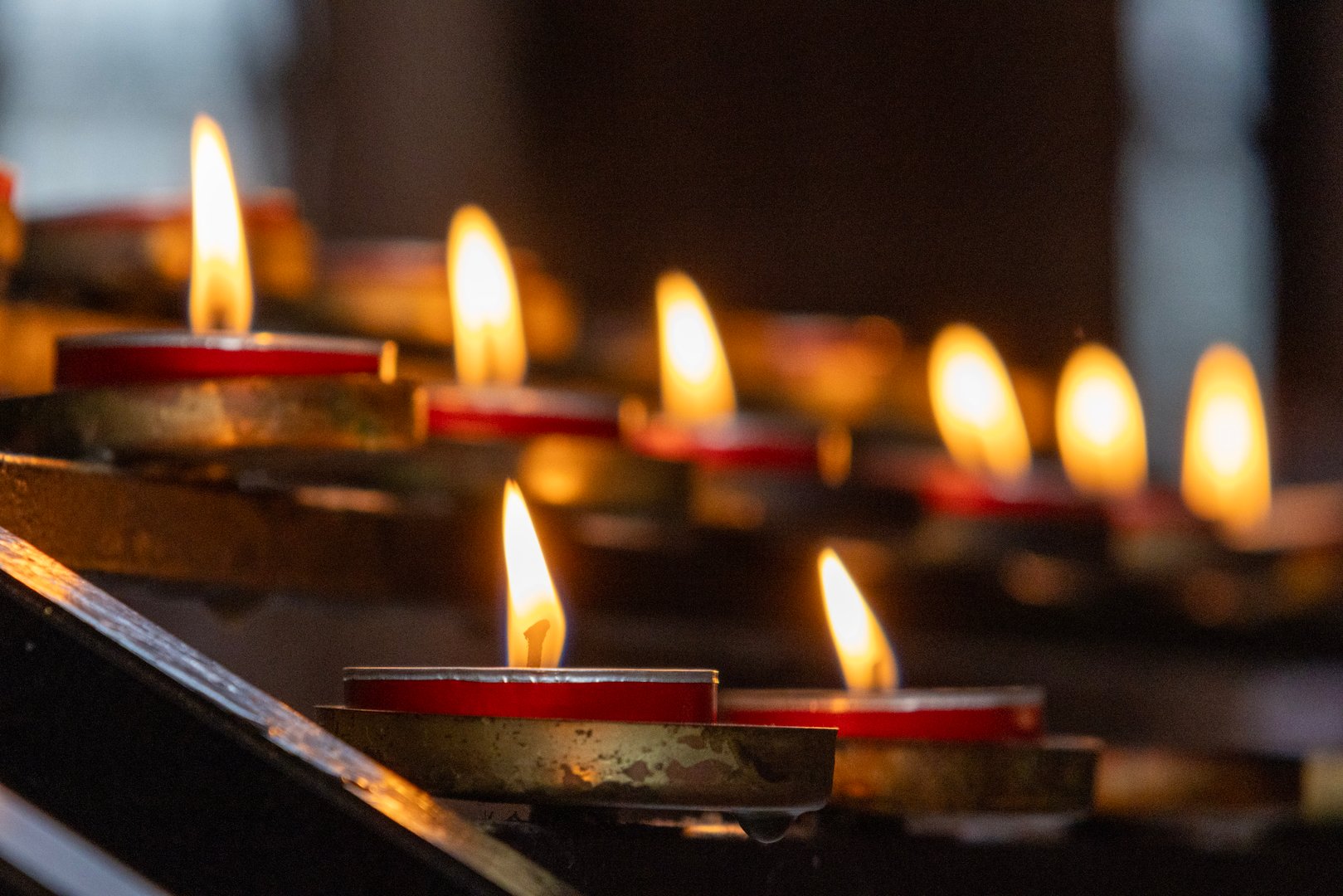 A selective focus photograph of votive candles inside Manchester Cathedral. The candles have been lit by worshippers and visitors to the cathedral. The photograph was created on a fine autumn day in Manchester, Northwest England
