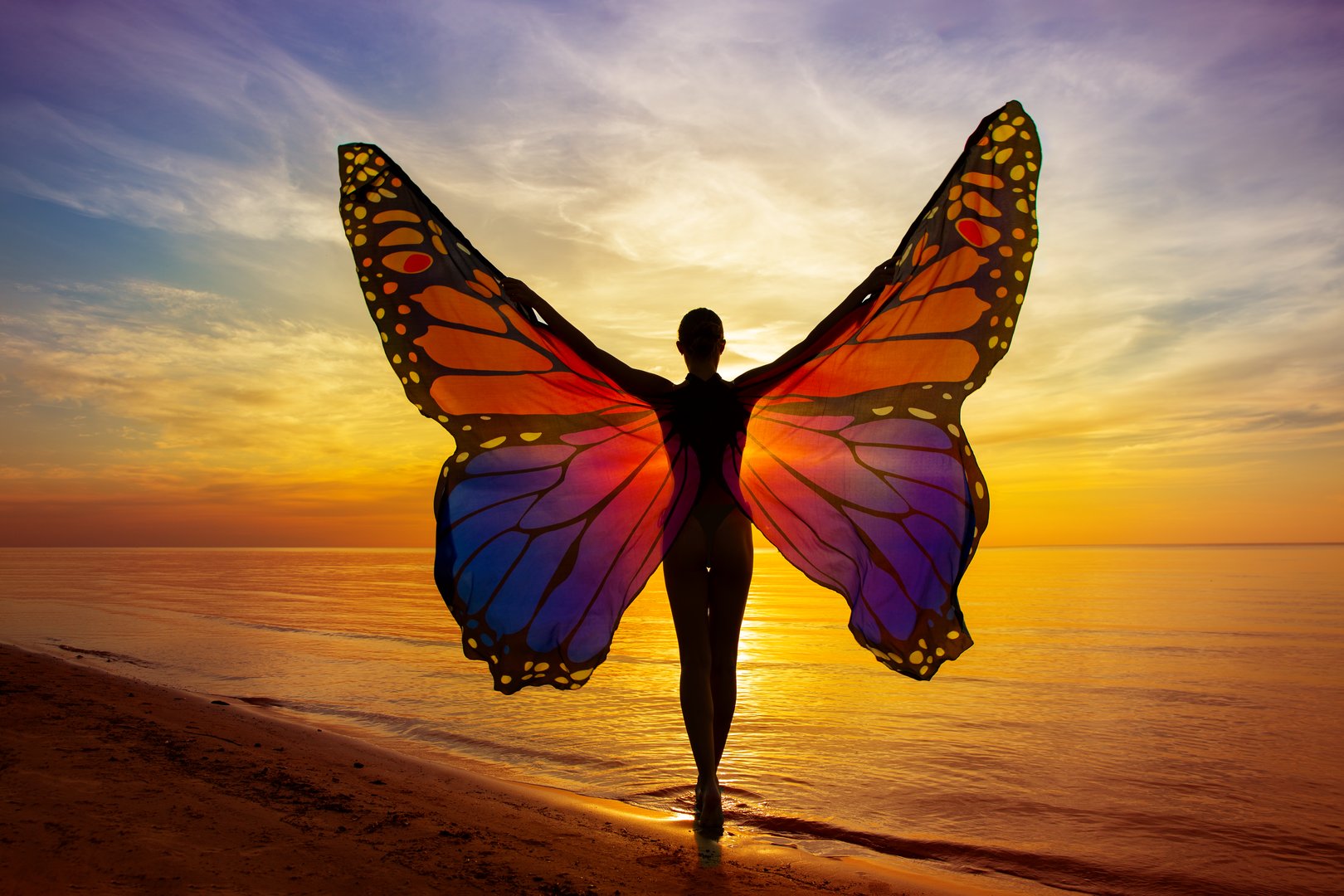 Graceful Woman with Vibrant Butterfly Wings on the Beach at Sunset Sunshine. Magical Mood of Transformation. Healing Meditation. Rear View of Girl Silhouette with Open Arms at Colorful Sea and Sky view