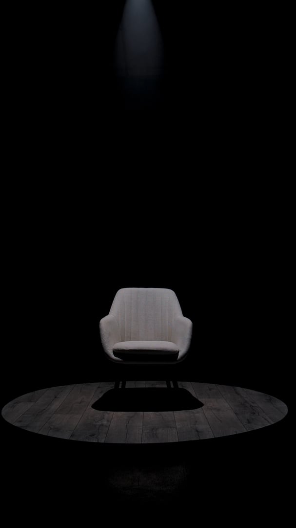 A sleek modern armchair is illuminated in a dark room, emphasizing its elegant contours and minimalist design with a spotlight