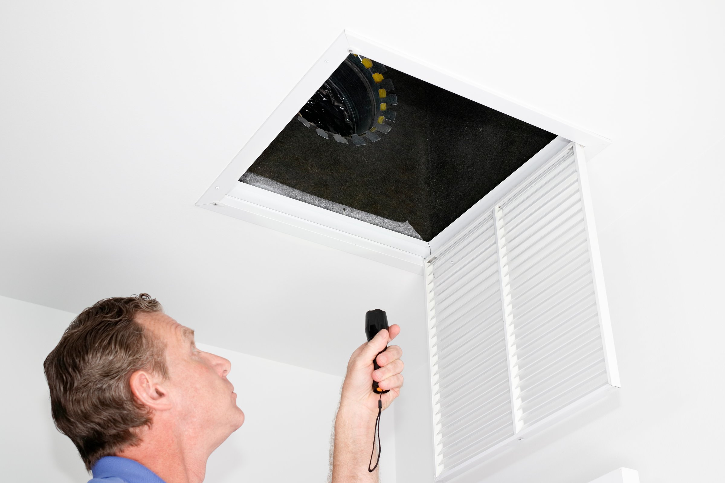 Male looking up into a ceiling air intake duct with a flashlight checking for maintenance. Person with a flashlight examining with a square opening of a home HVAC system