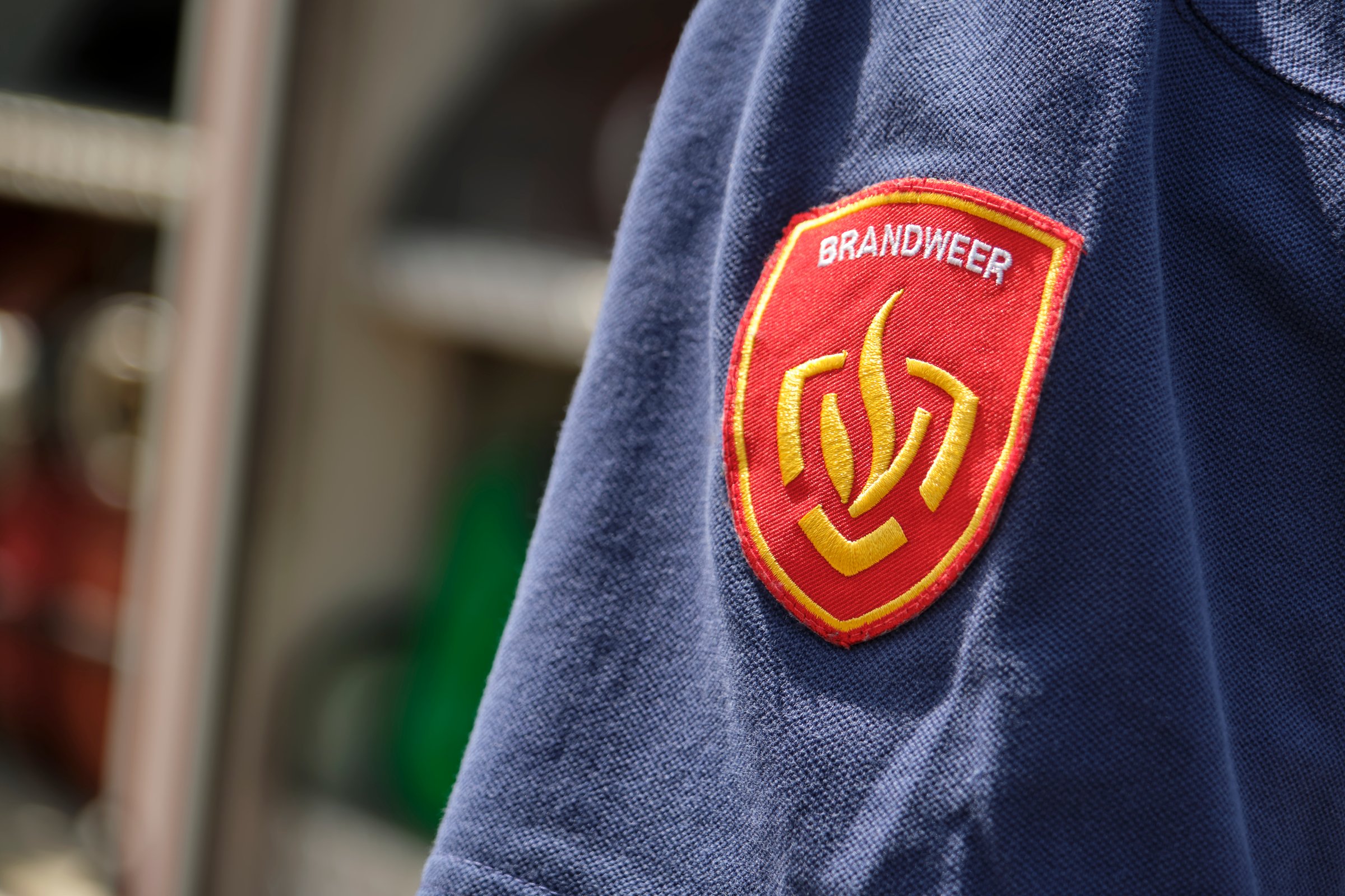 Dutch fire department badge on a firefighter's shirt. Dutch gold and red embroidered fire department logo on shoulder part of a blue shirt.