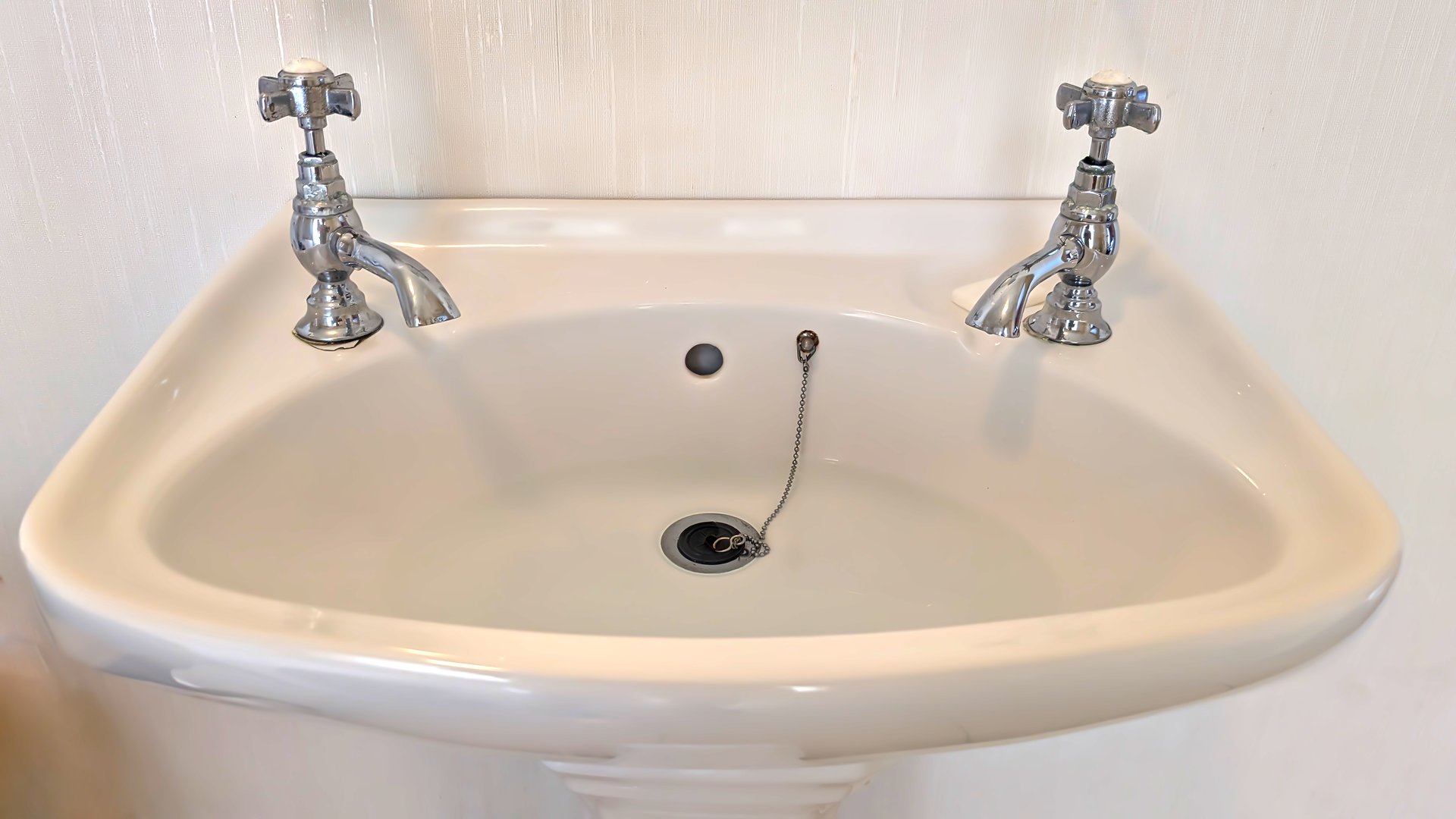 A Traditional English styled bathroom sink with two faucets and sink plug for water economy.