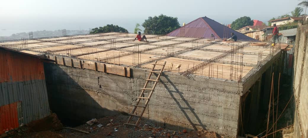 Construction site with concrete walls, wooden scaffolding, and a worker near the center. Partially completed building structure.