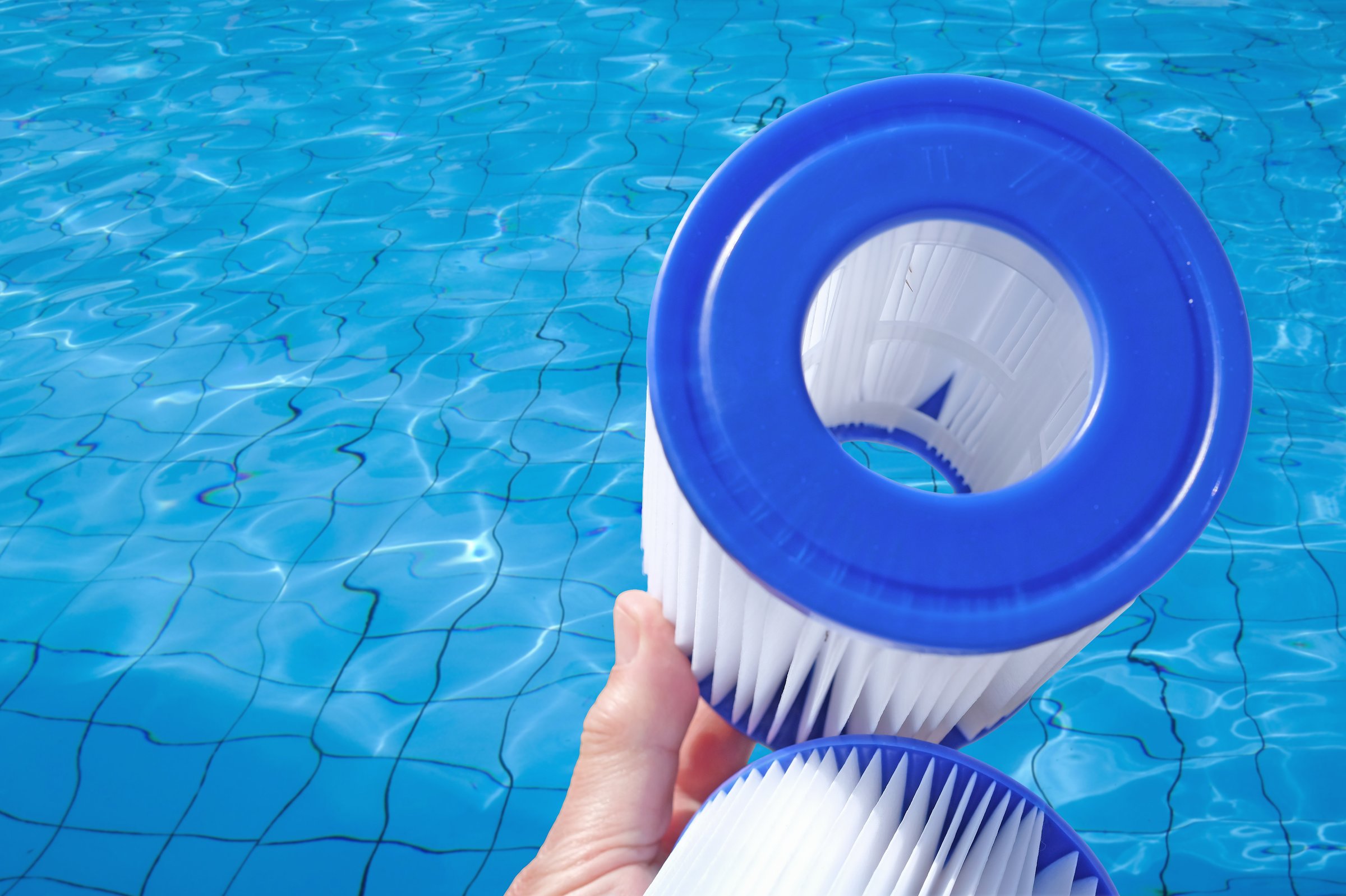 Reusable pool cartridge filters are in a human hand on pool water backdrop. Cleaning and maintenance, water filter replacement.