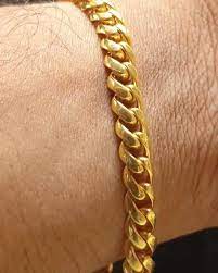 Close-up of a gold chain bracelet on a person's wrist against a beige skin tone background.
