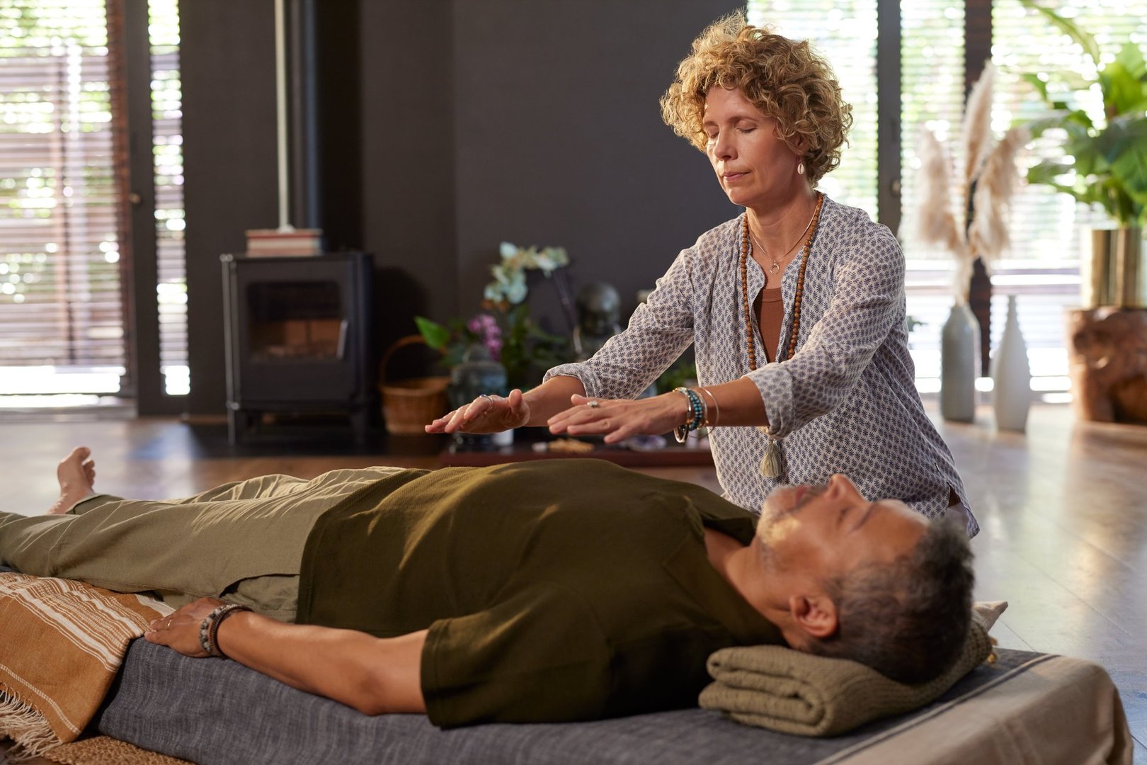 Woman performing reiki energy healing on man at wellness center. Holistic therapist holding hands above body client to restore balance and calm. Peaceful session focused on mindfulness, energy flow, and deep relaxation with reiki therapy.