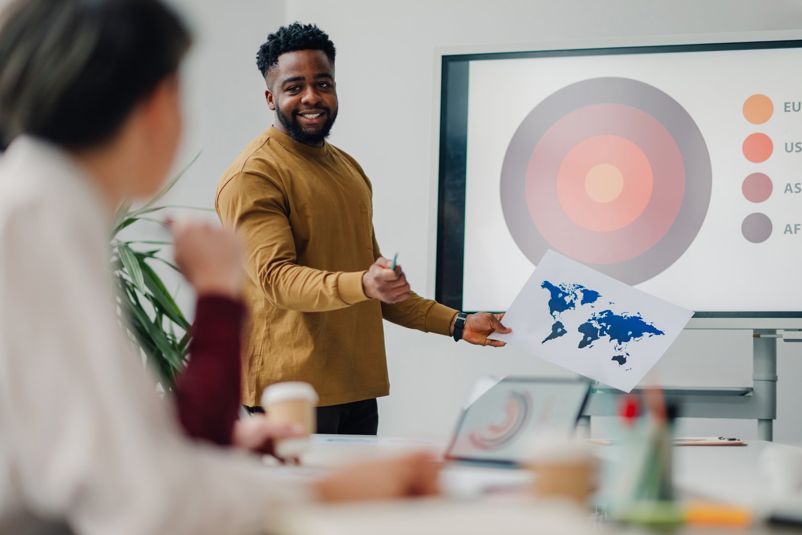 Young businessman holding world map explaining global marketing strategy during a meeting with his team