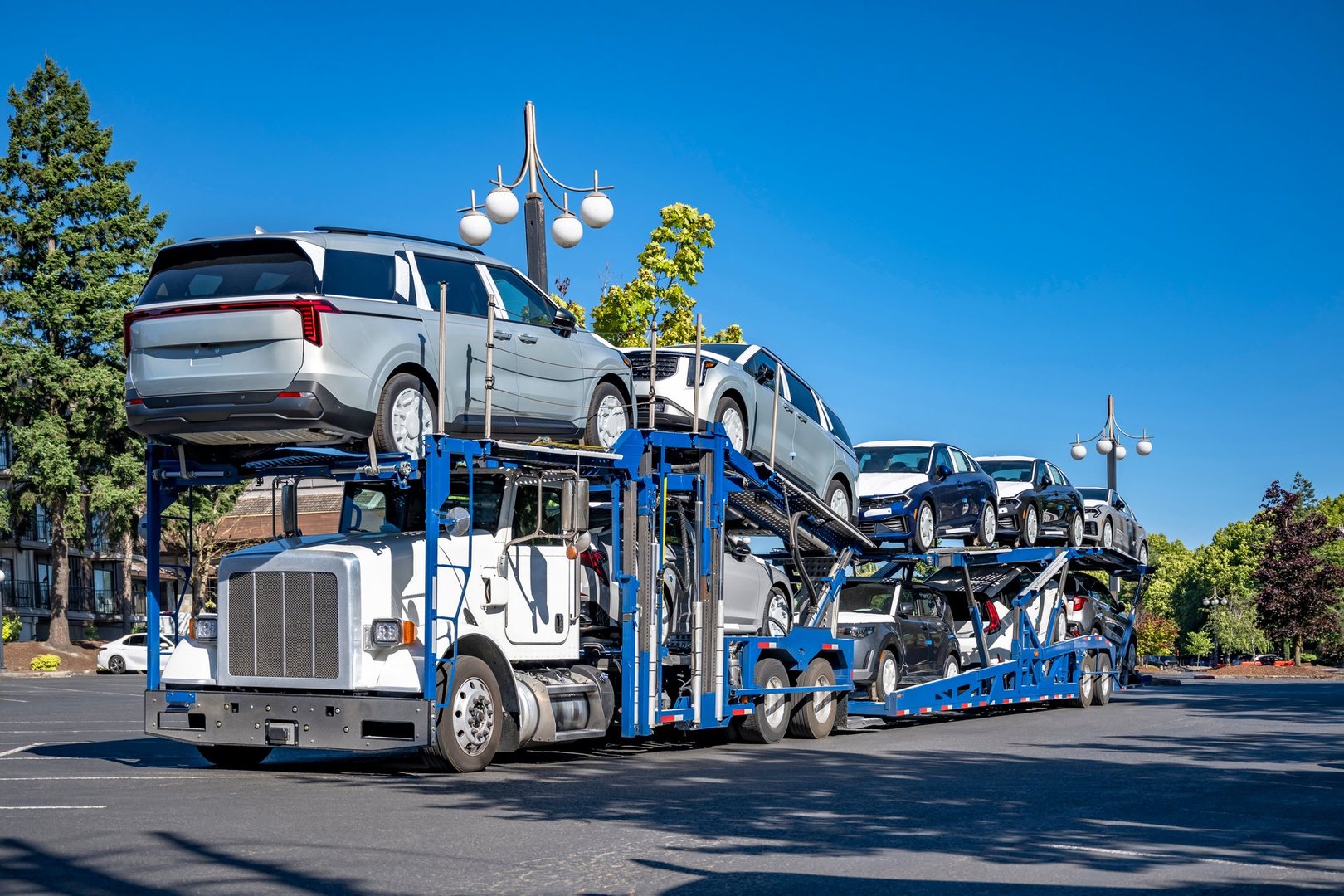 White industrial standard big rig bonnet car hauler semi truck tractor with two level loaded modular semi trailers standing on the industrial parking lot taking a break at sunny day