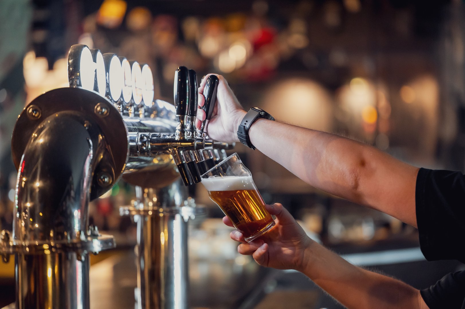 A bartender pouring a golden beer from a modern tap into a glass, showcasing the brewing process in a vibrant bar environment filled with soft lighting.
