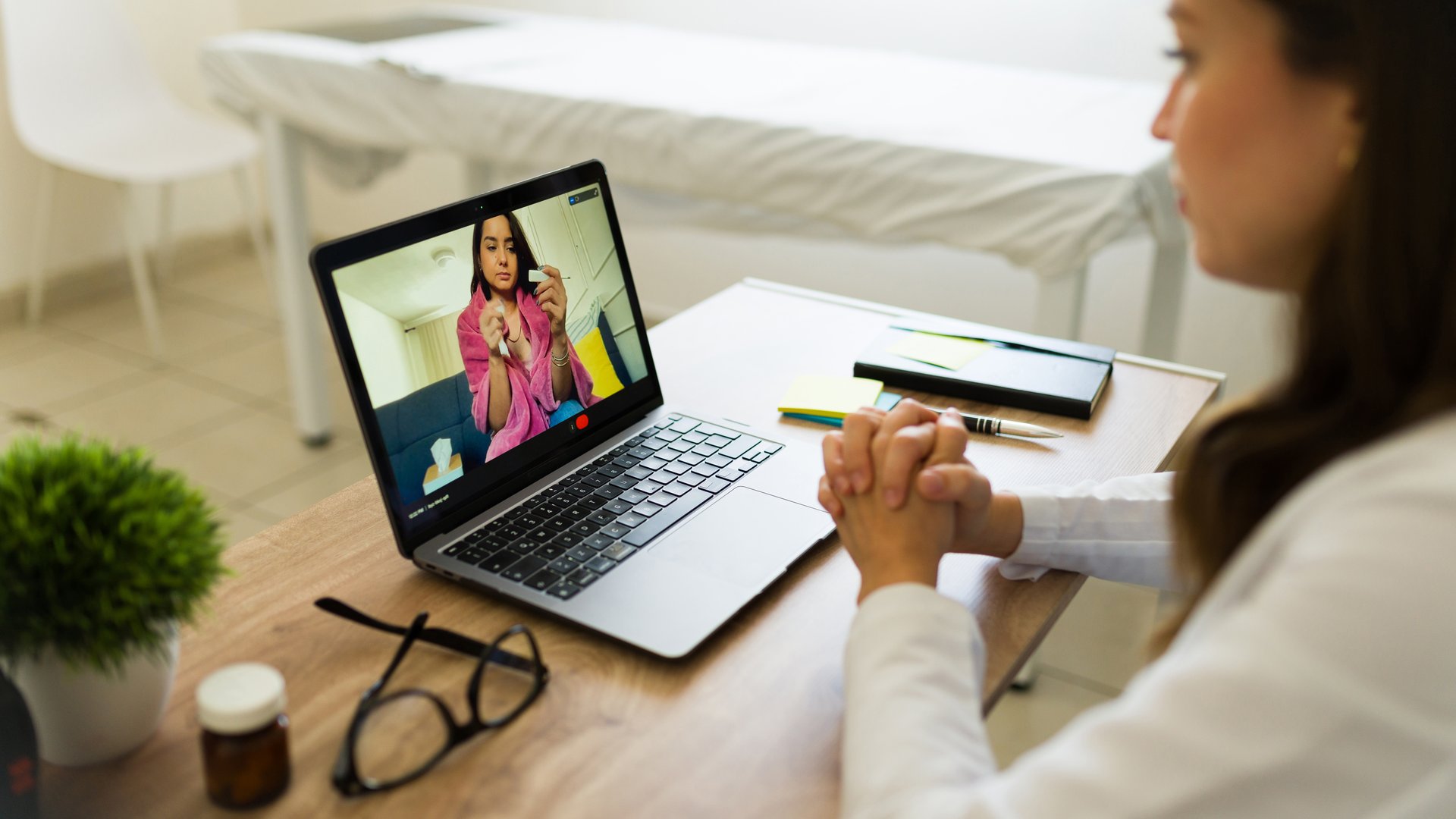 Doctor conducting a video call consultation with a patient and displaying a thermometer to the camera while listening attentively