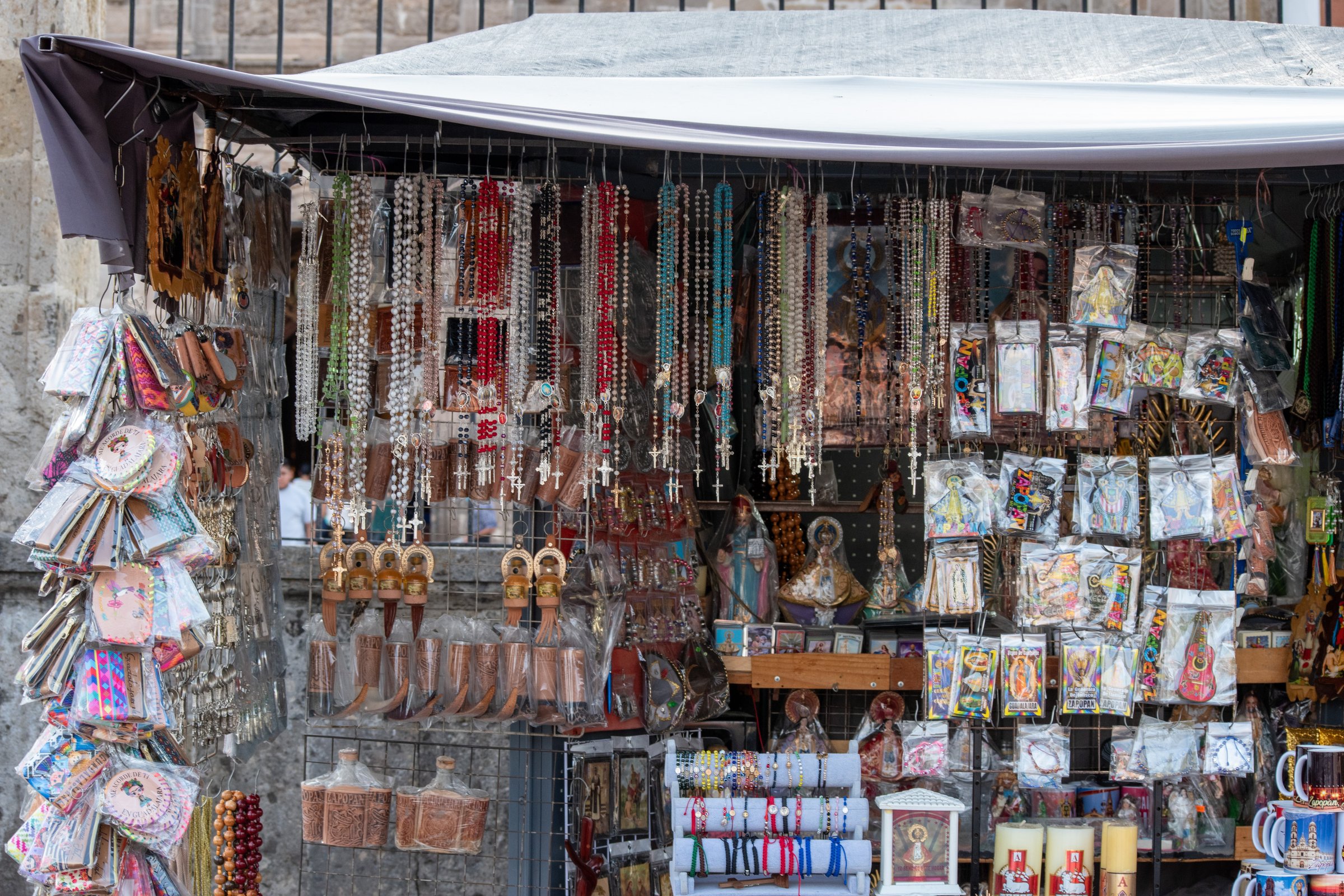 Zapopan, Mexico - June 5 2025: Catholic-themed street stand displaying rosaries, saints, candles, bracelets, and prints in central square of Zapopan, Jalisco
