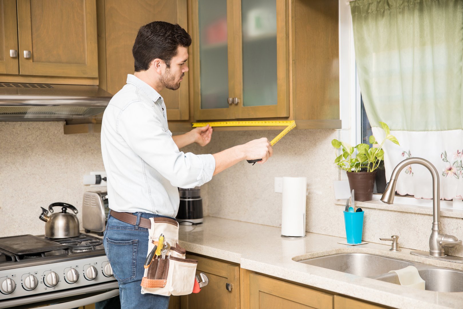 Young handyman using a tape measure to get the dimensions of a kitchen cabinet and do some repairs