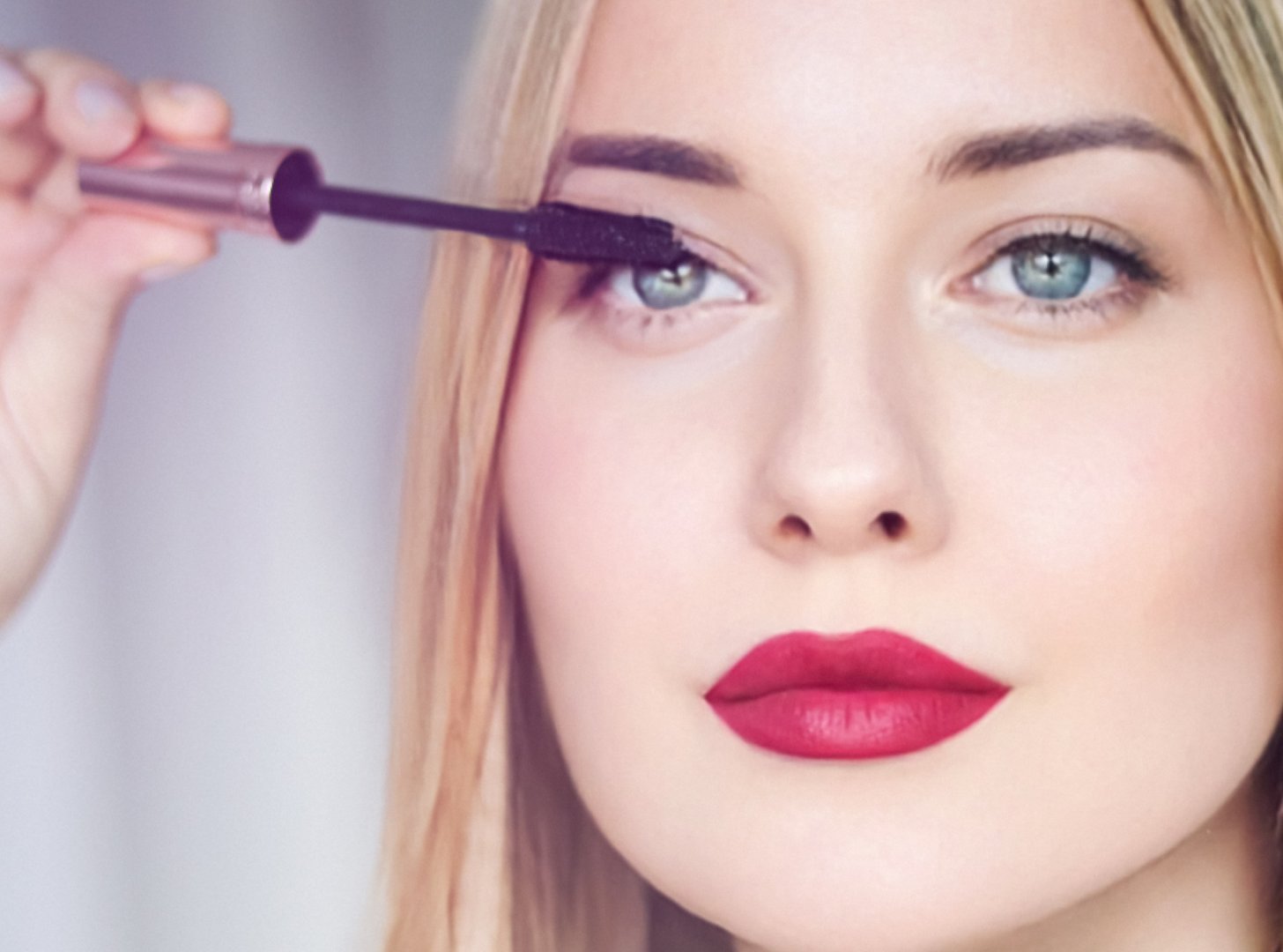 Woman applying mascara with confidence, defined brows and red lipstick
