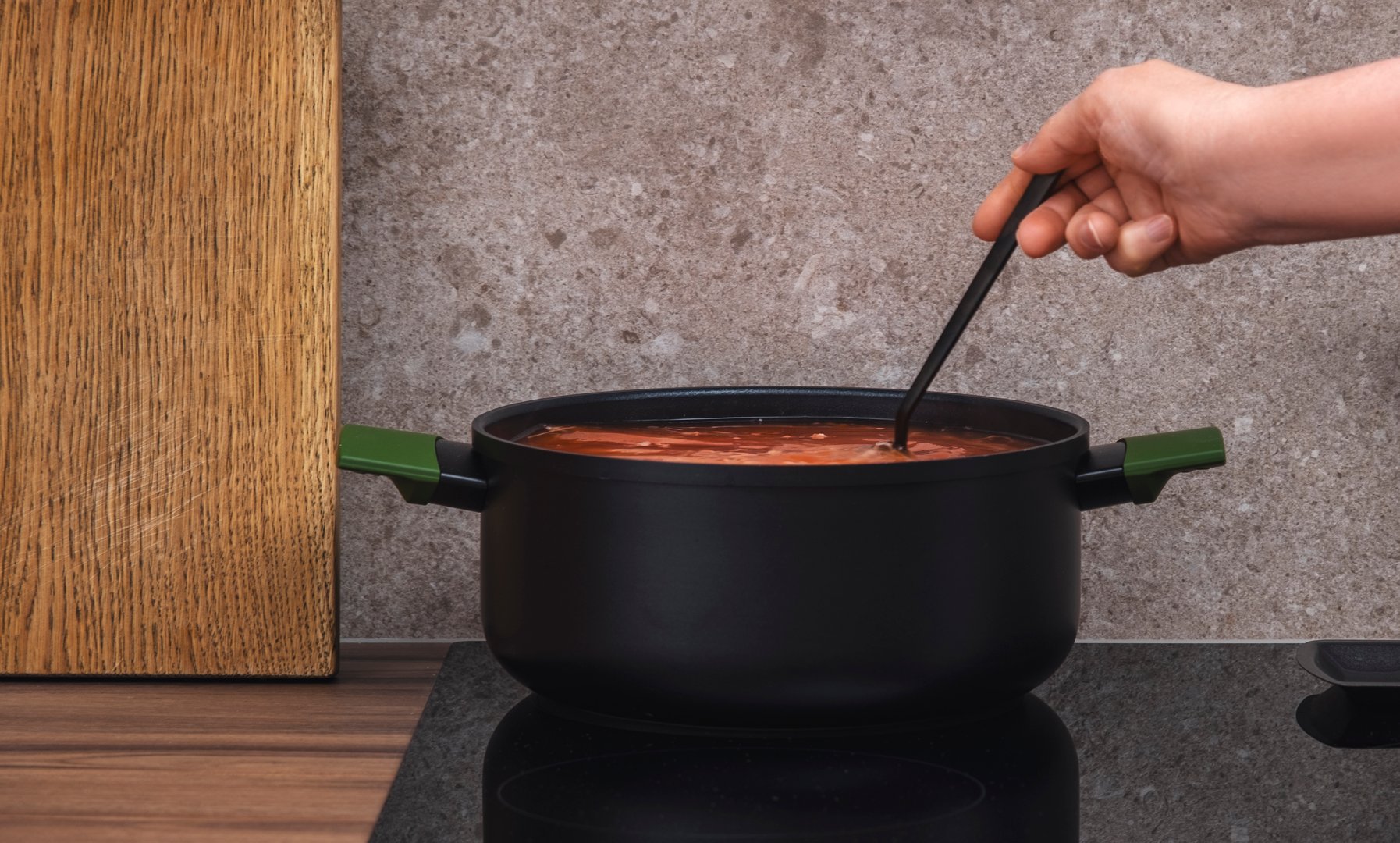 Female hand stirring vegetable soup in large black saucepan on induction hob in modern kitchen