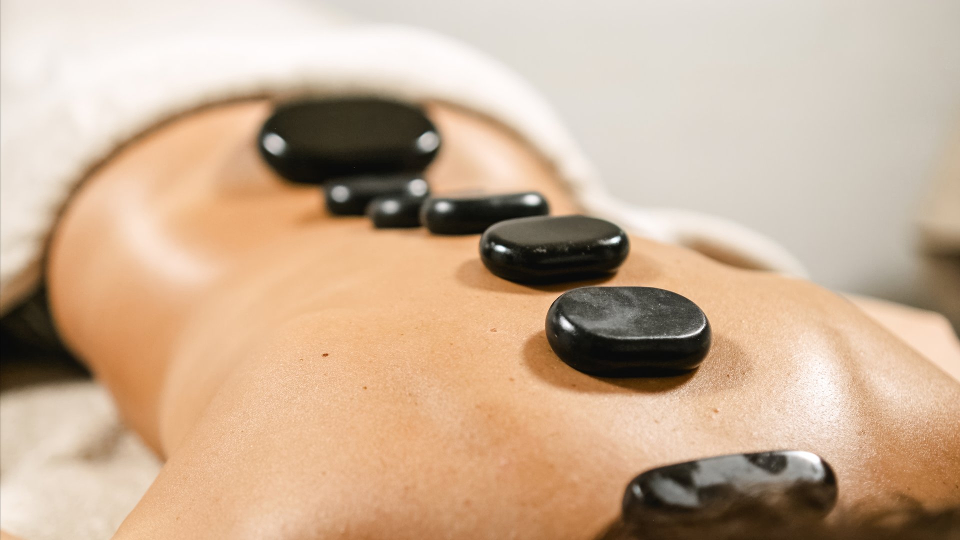 Black massage stones placed on woman's back during a hot stone therapy session, providing relaxation and healing
