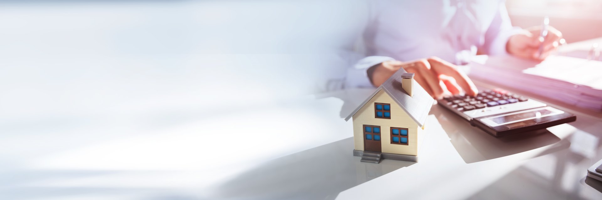 Close-up Of A Person Hand Doing Property Tax Calculation With House Model On The Table