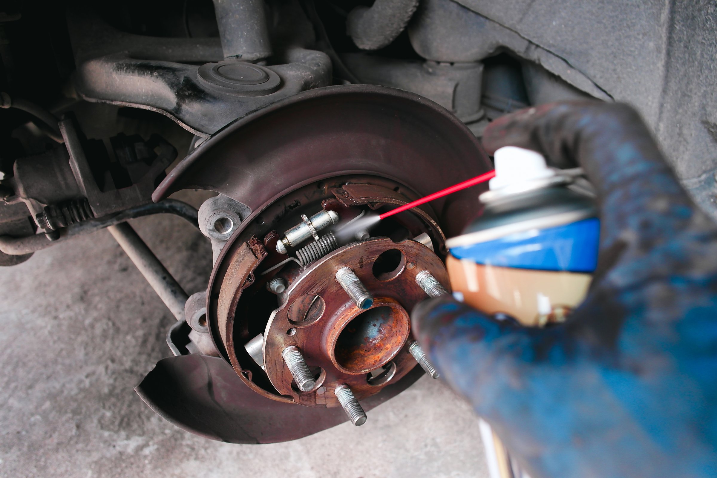 A mechanic cleans a dust the inside of a car brake drum with cleaning spray. Car brake maintenance concept