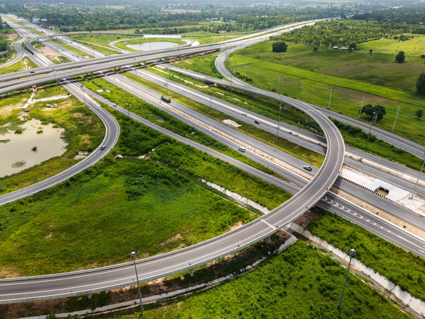 Drone shot a large highway interchange crossing over green farmlands in Thailand. The layered roads and ramps highlight modern transport infrastructure in a rural place