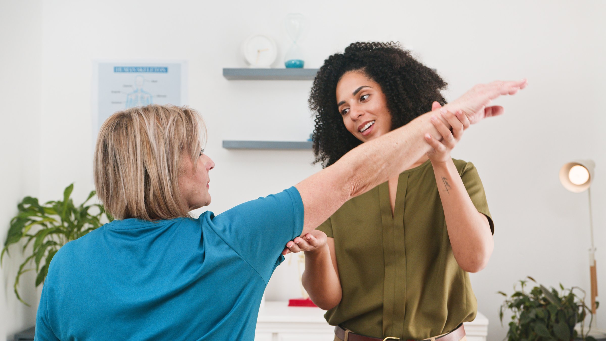 A friendly physiotherapist guides a senior woman through a safe arm stretch, strengthening mobility and flexibility. The hands-on session takes place in a bright clinic, highlighting care and personalized rehabilitation.