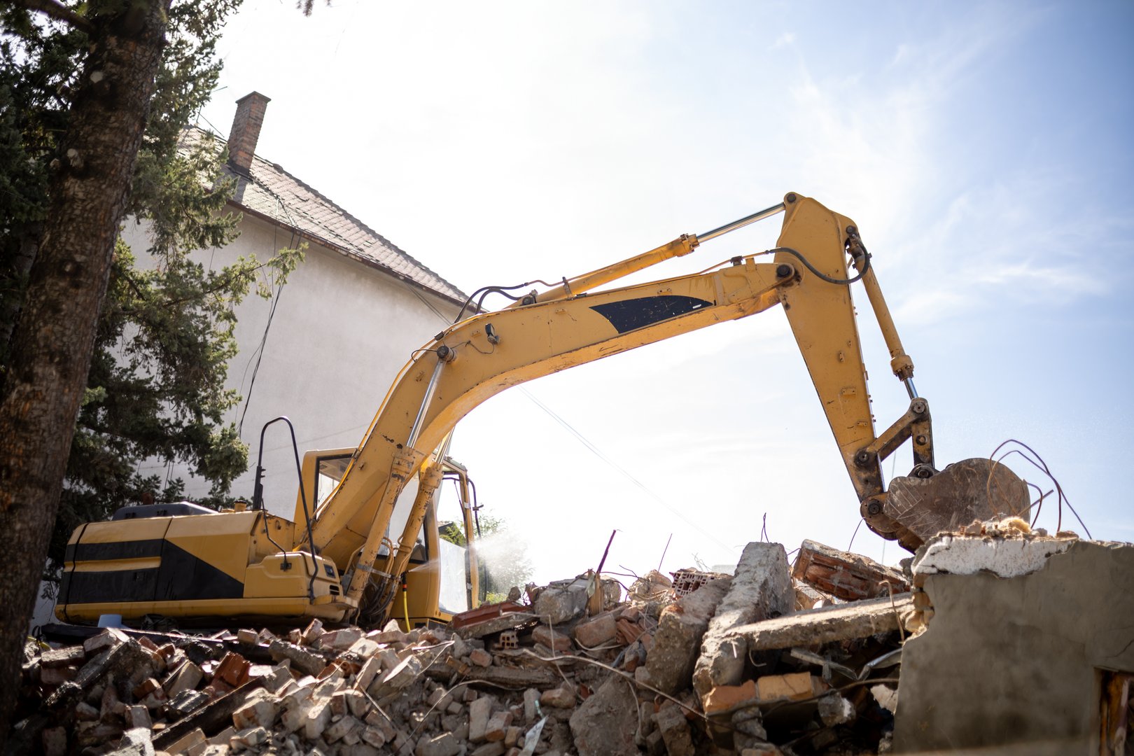 Heavy machinery is actively clearing rubble from a construction site located in an urban neighborhood under clear skies, showcasing ongoing building efforts.
