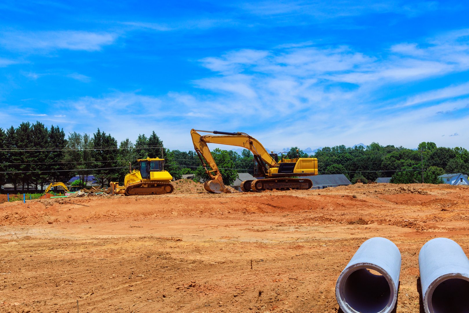 Heavy machinery are actively digging moving earth at construction site clear blue sky enhances vibrant scene of land development.