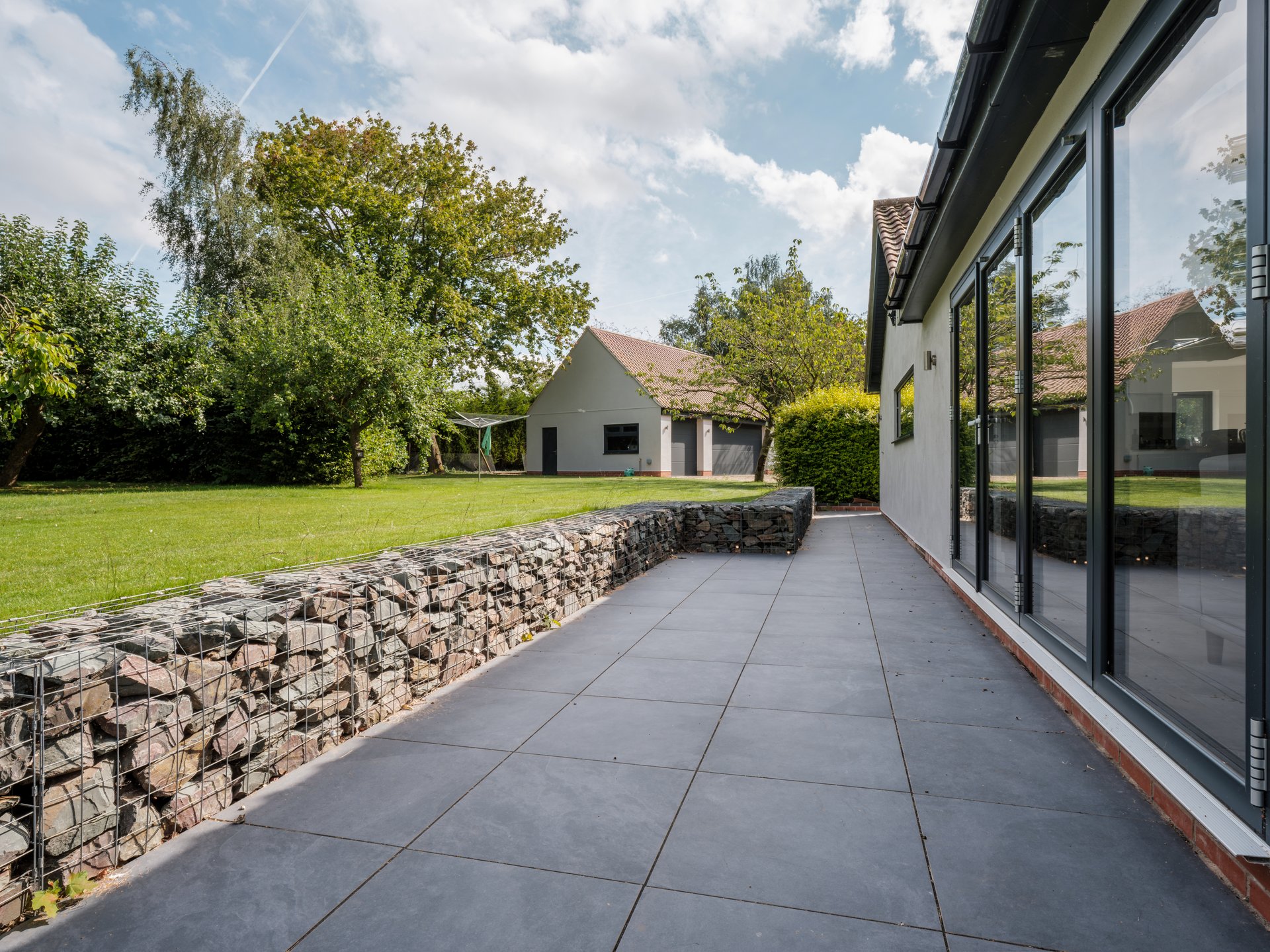 Luxury home with bifold doors leading to contemporary landscaped gardens with patio and gabian walls