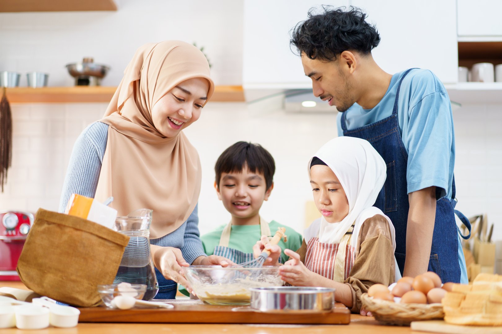 Asian Muslim family, consisting of a father, mother, son, and daughter, is enjoying cooking together. In a close-up shot, the Muslim woman is kneading dough with her daughter to bake bread.