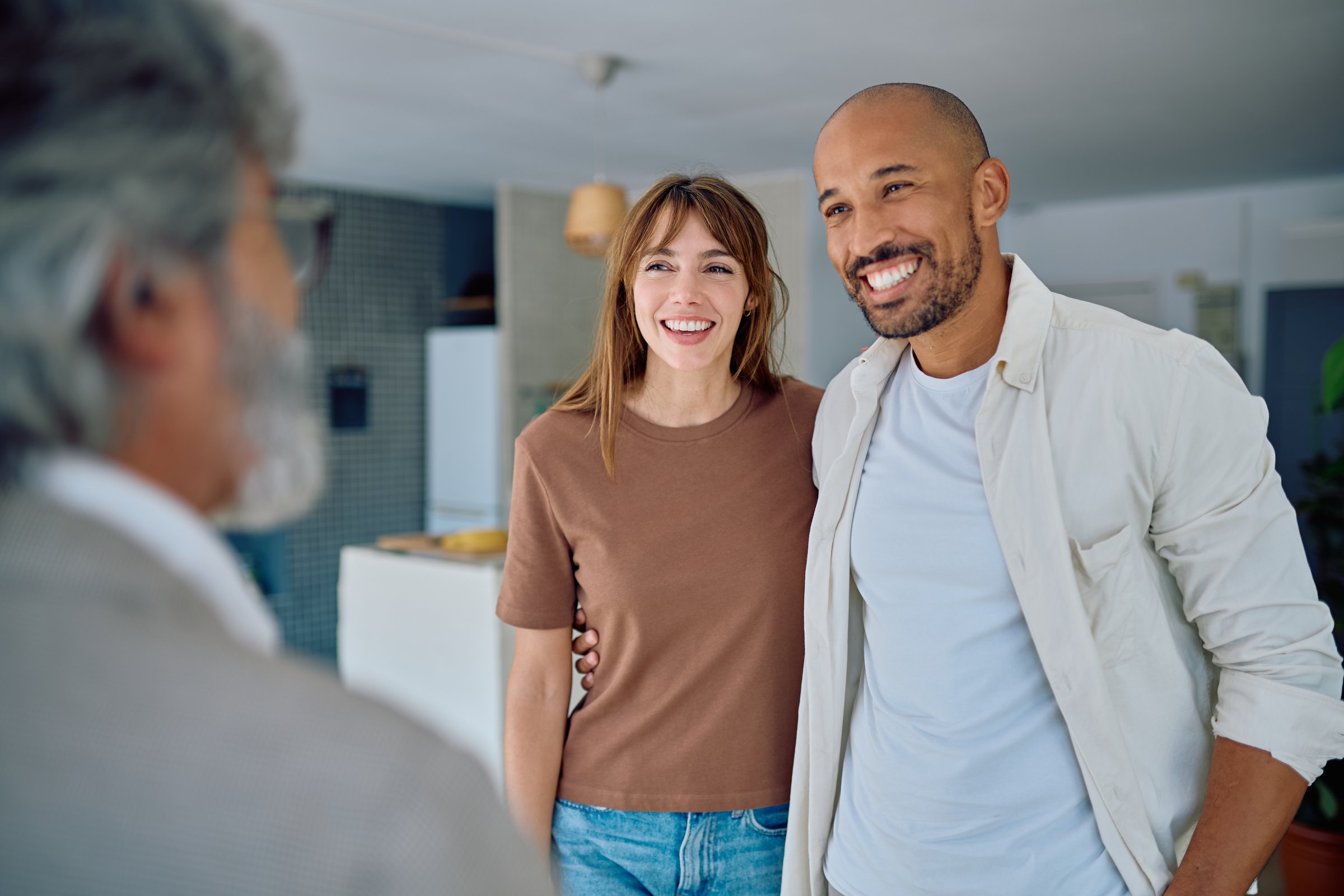 Young couple smiling and engaging in conversation with a real estate agent while exploring a new house for potential purchase