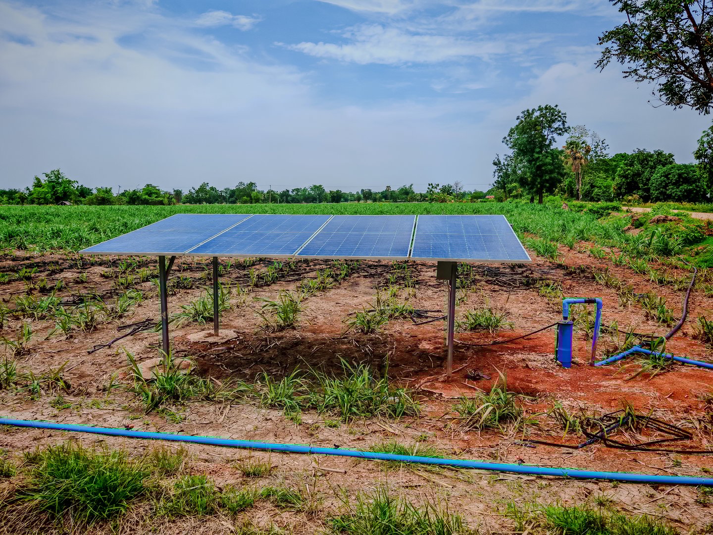 Solar panels installed in a field to pump groundwater for agricultural purposes. The setup includes solar panels, a pump, and piping, demonstrating sustainable energy use in farming.