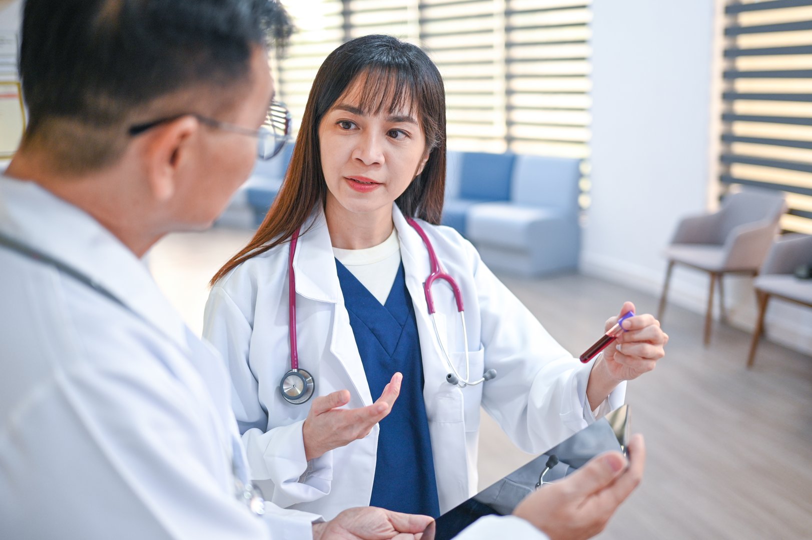 Focused on precision, two healthcare professionals study a test tube blood sample, using digital tools to assist in their medical examination