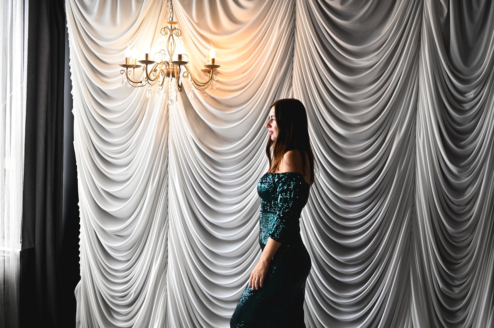 Elegant woman posing in a luxurious room with draped curtains and chandelier