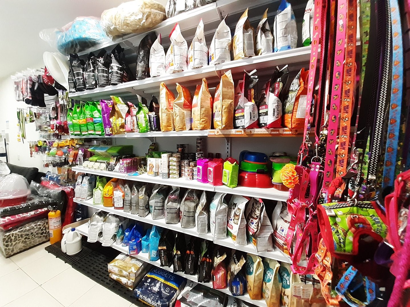 Pet store aisle with shelves of pet food, accessories, grooming items, and colorful leashes on display.