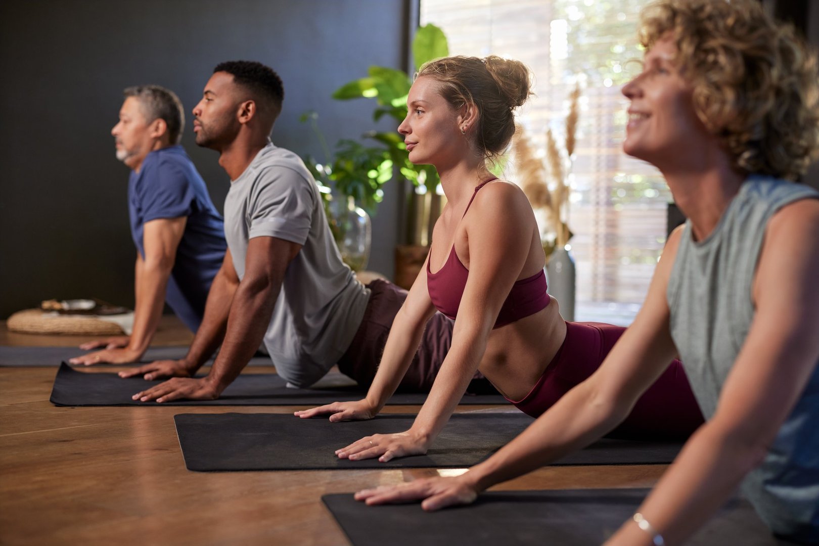 Diverse people doing yoga together in a bright indoor studio. Group of multiethnic adults practicing upward facing dog pose during a yoga session. Focused and calm women and men in a row stretching on yoga mats in a wellness center.
