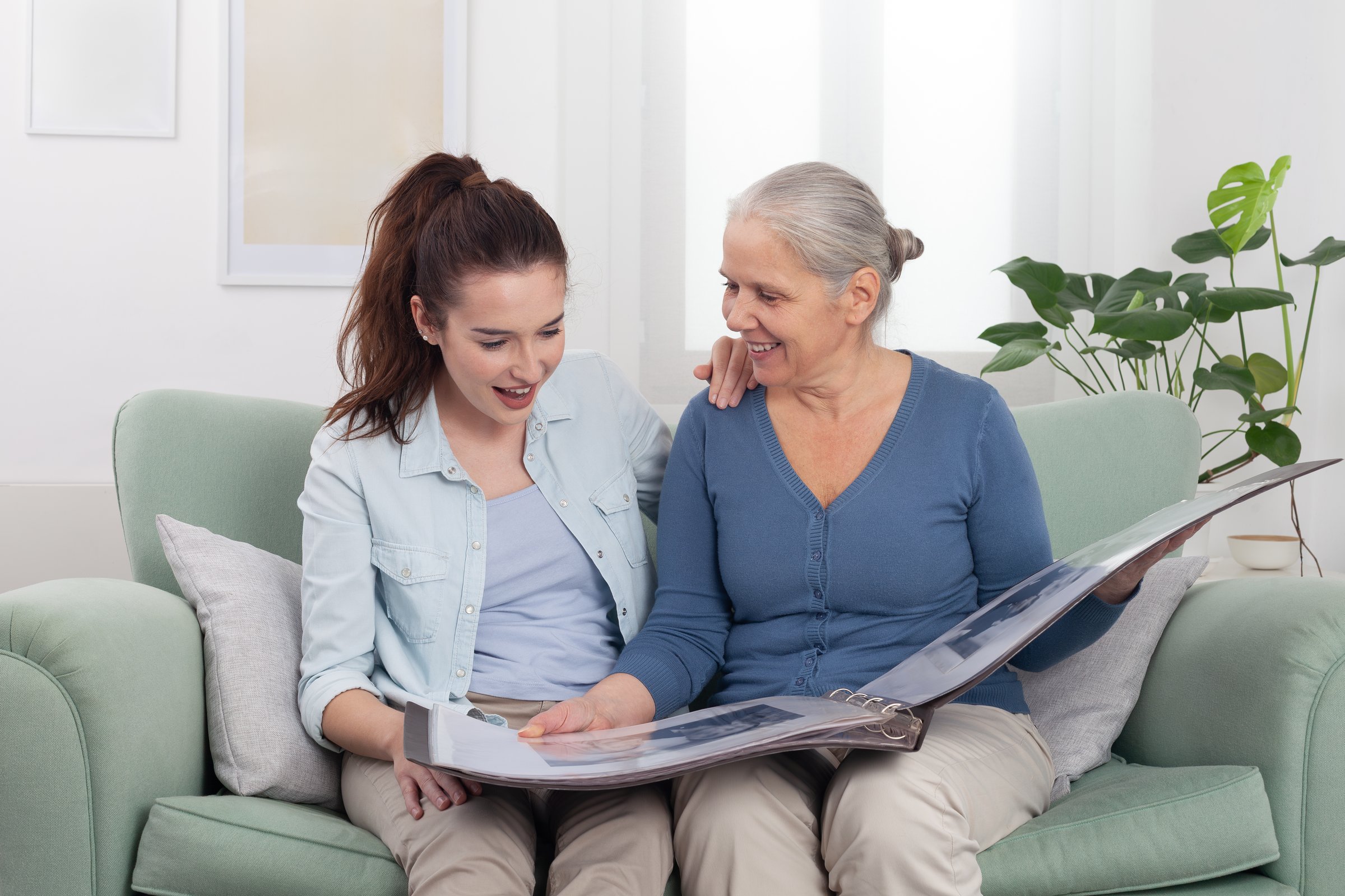 Joyful elderly grandmother sharing memories with her smiling granddaughter as they look through an old photo album together. A family moment full of connection, nostalgia, and generational bonding