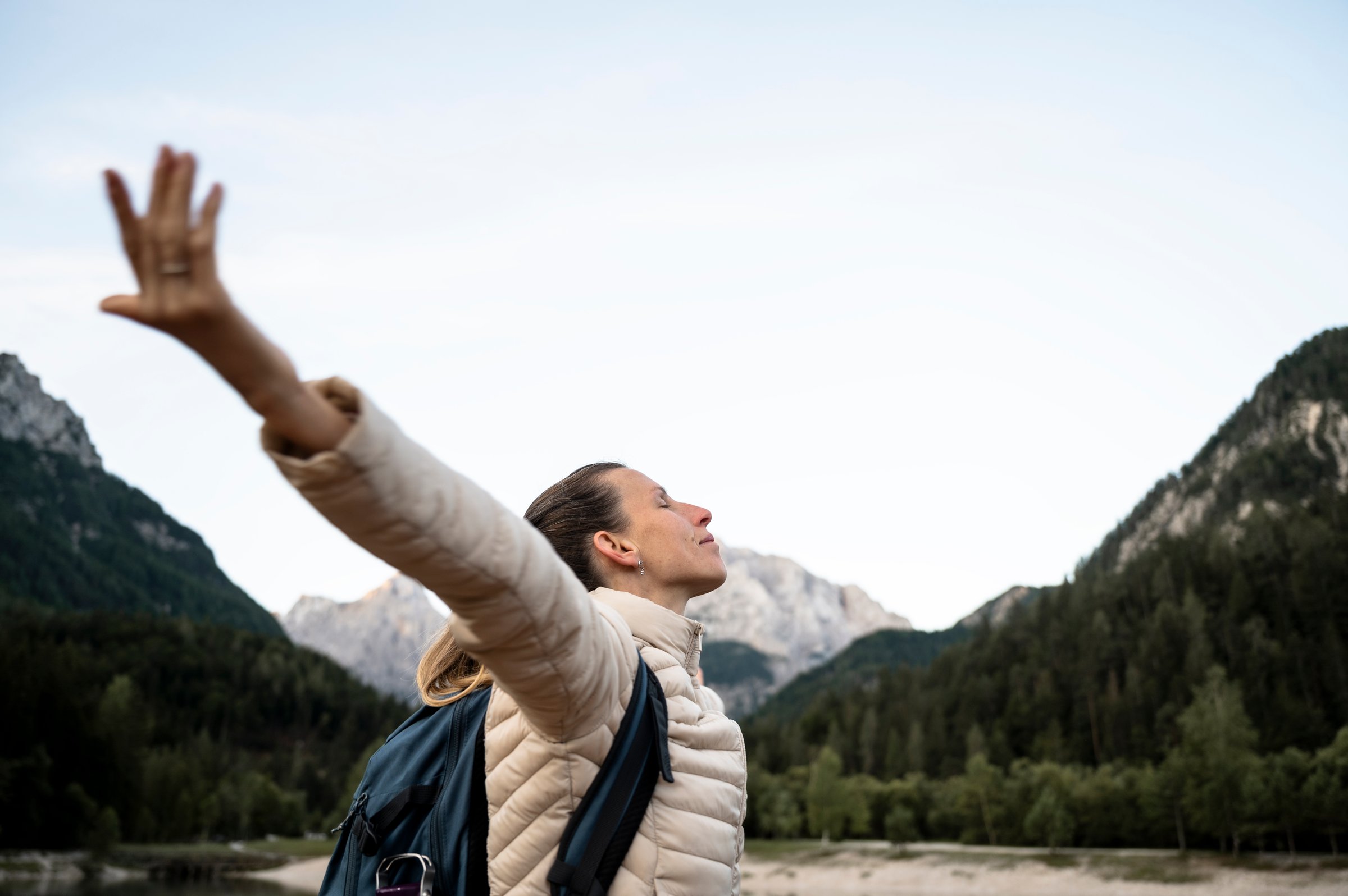Profile view of a young woman, a hiker, standing in the middle of beautiful mountain nature with her arms spread widely, enjoying her life.