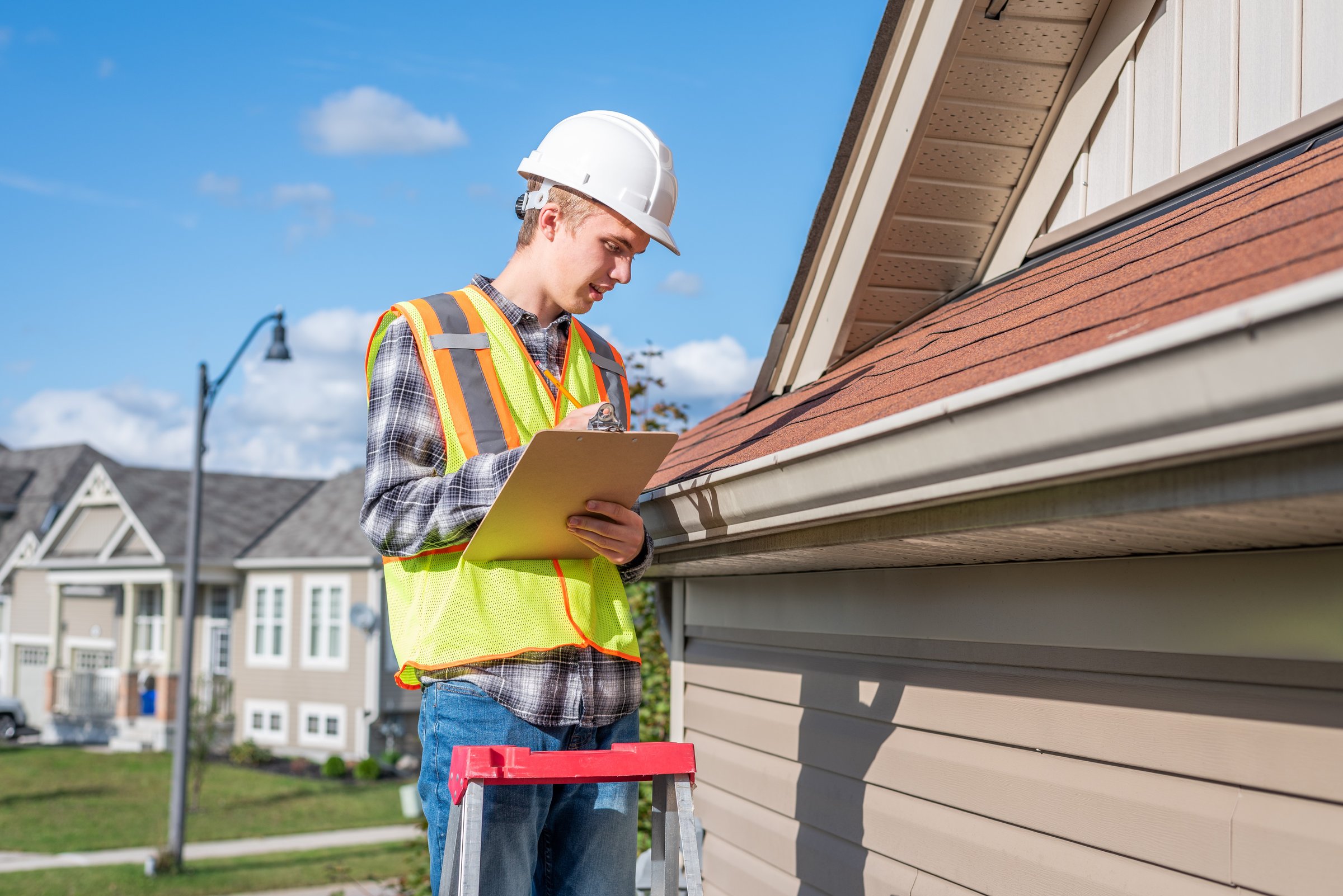 Roof maintenance inspection by a professional in safety gear, checking shingles and gutters on a residential building in Anchorage, Alaska.