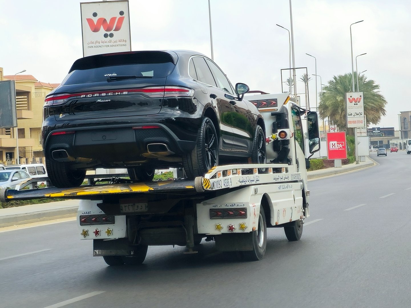 Cairo, Egypt, April 27 2024: A tow recovery transporter hydraulic flatbed truck with a Porsche Macan new car, a compact luxury crossover SUV (D-segment) produced by German manufacturer Porsche, selective focus