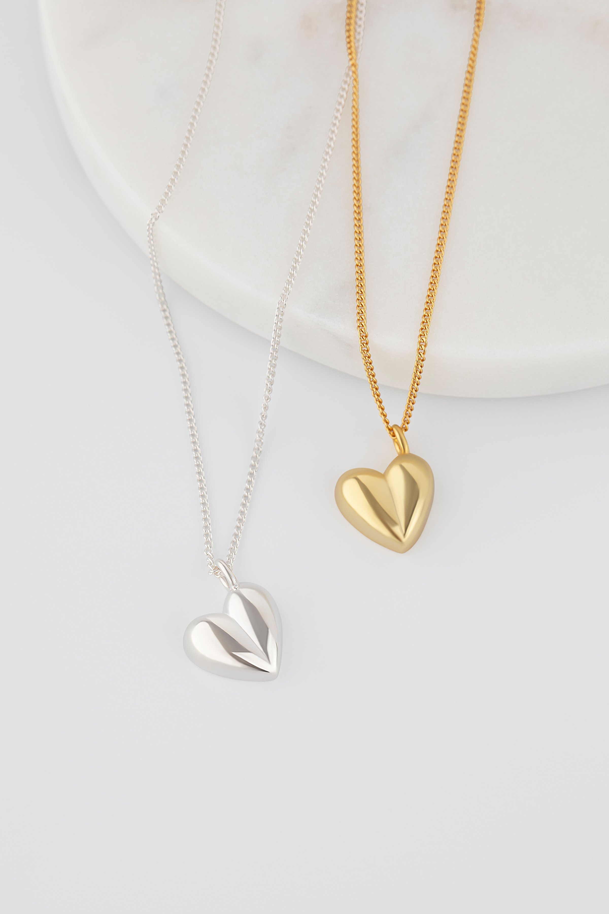 Elegant gold and silver heart-shaped necklaces on white marble display. Catalog of jewellery
