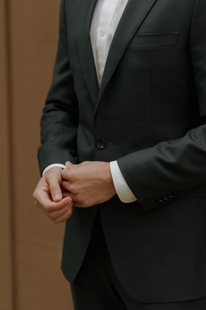 Close-up of a man in a dark green suit adjusting his cufflinks.