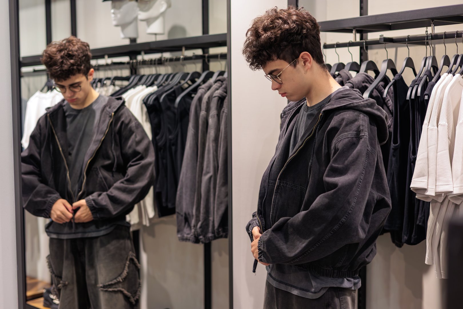 Teen boy trying on black denim jacket in clothing store, looking at reflection in mirror, concept of fashion, shopping, teen lifestyle and self-expression. shopping, style choice and identity.
