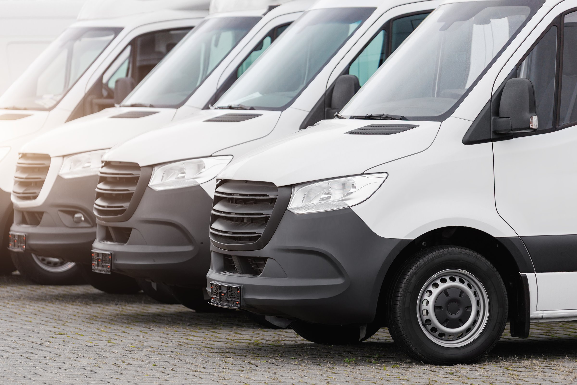 Fleet new modern electric hybrid hydrogen or diesel white vans parked in line row outdoors. Cargo freight industrial courier transportation logistics service. Commercial vehicle maintenance insurance.