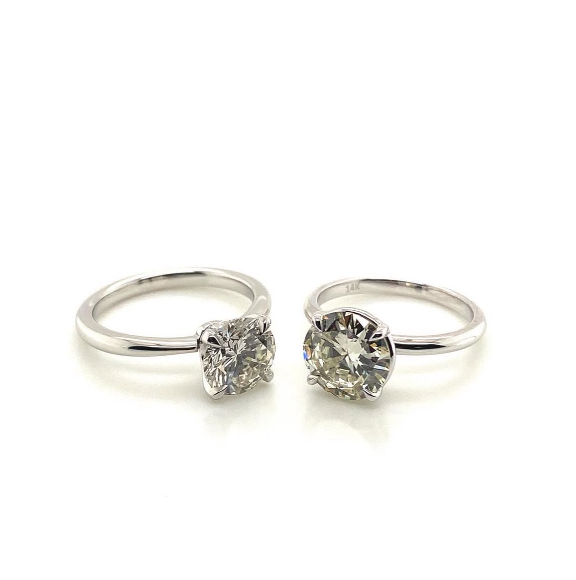 Two silver engagement rings with large round diamonds on white background.