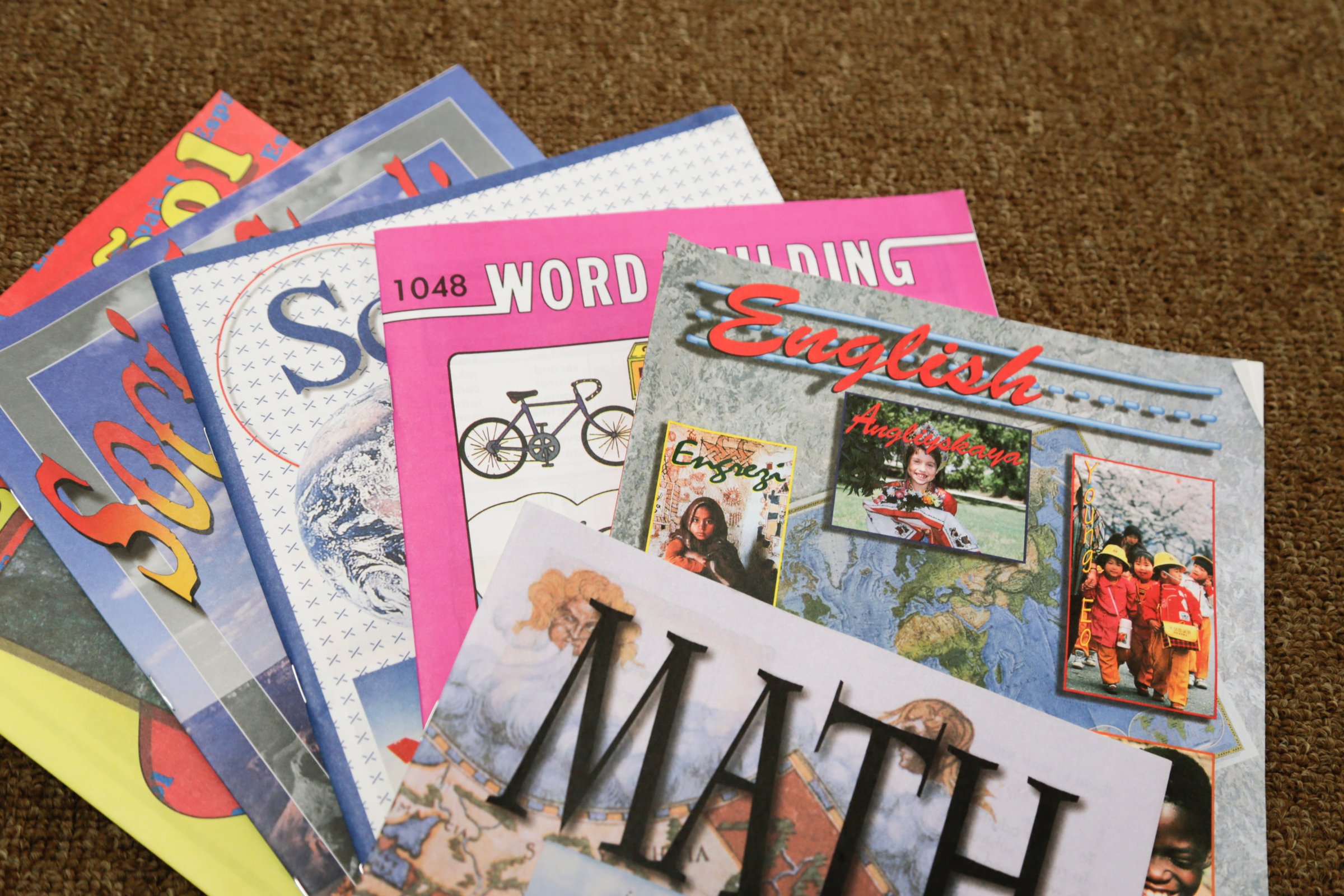 A collection of colorful educational workbooks on subjects like math and English, laid out on a brown carpet.