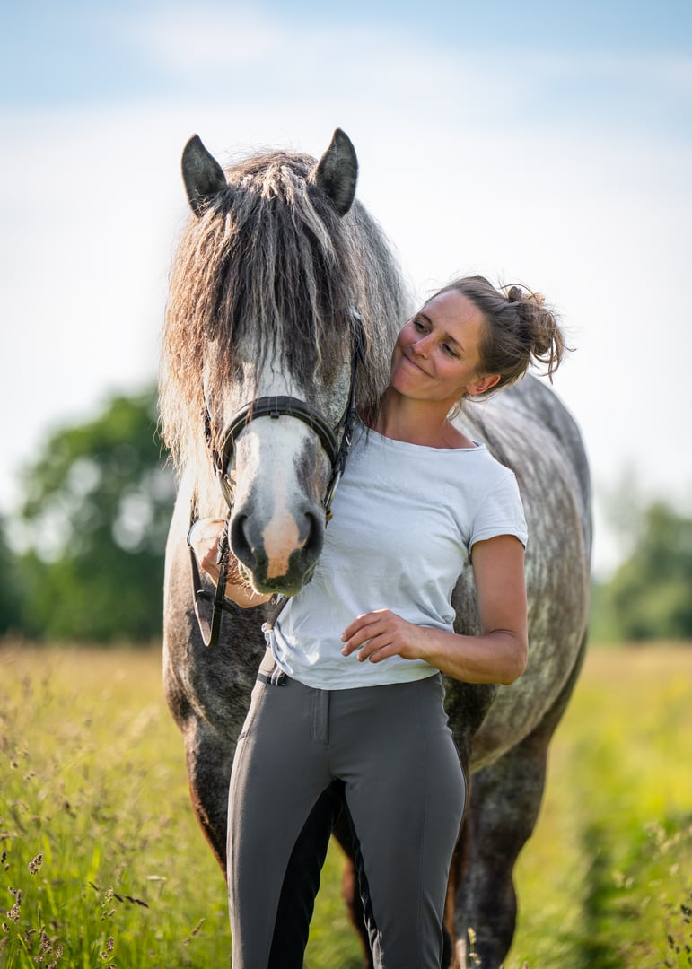Beautiful rider and her dapple gray horse share a tender hug on a quiet country lane. An authentic moment of love, trust, and emotional connection in a natural rural setting.