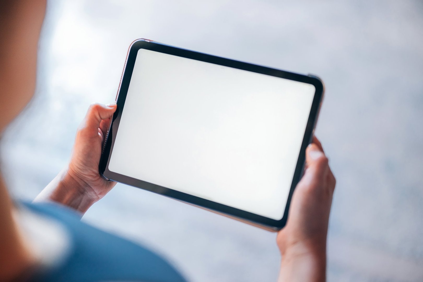 Close-up view of a person holding a tablet with a blank screen, showcasing technology's versatility and usability. Perfect for presentations, app advertisements, or showcasing digital interface designs.