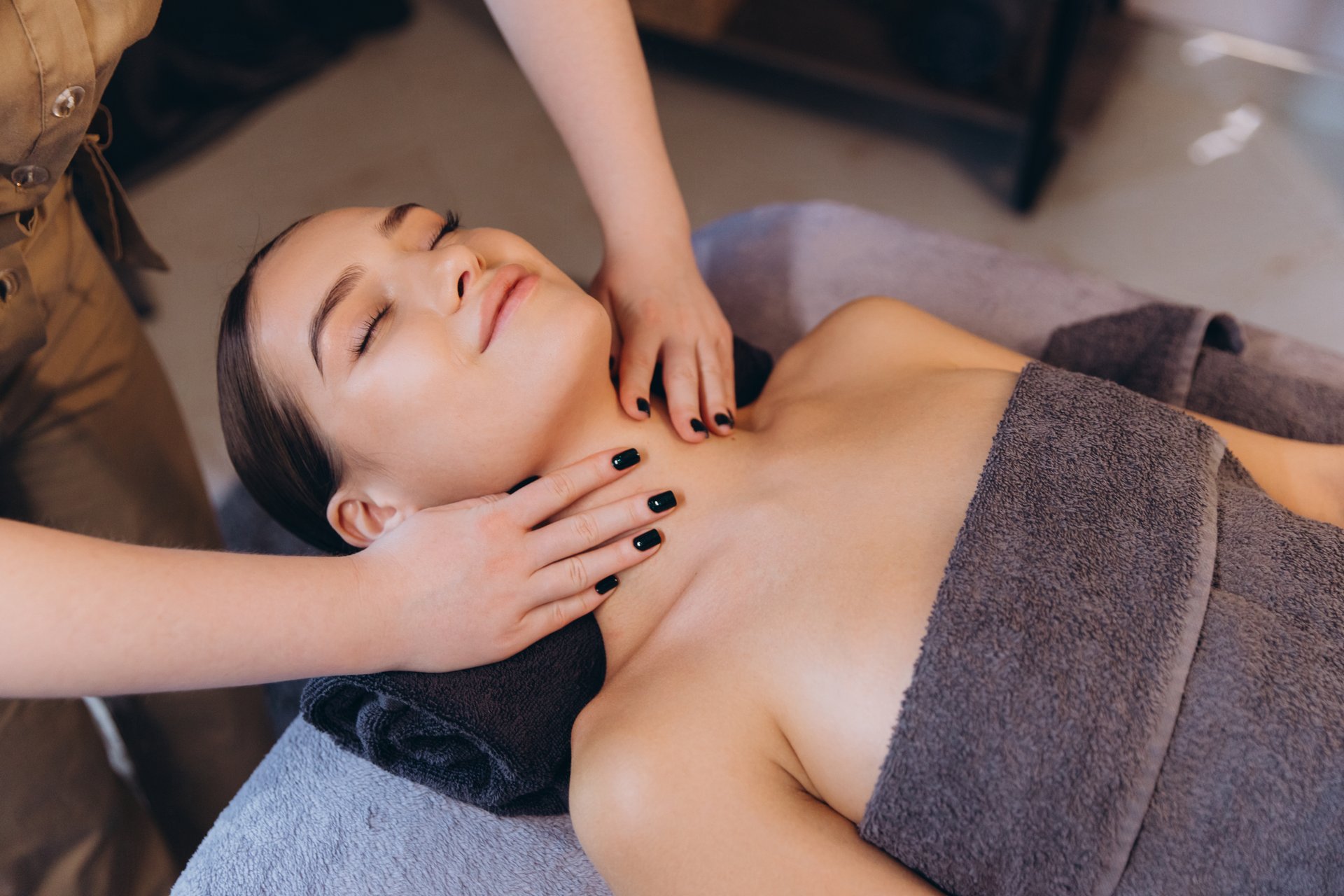 Masseuse massaging neck of young woman lying on massage table, enjoying relaxing treatment in spa salon