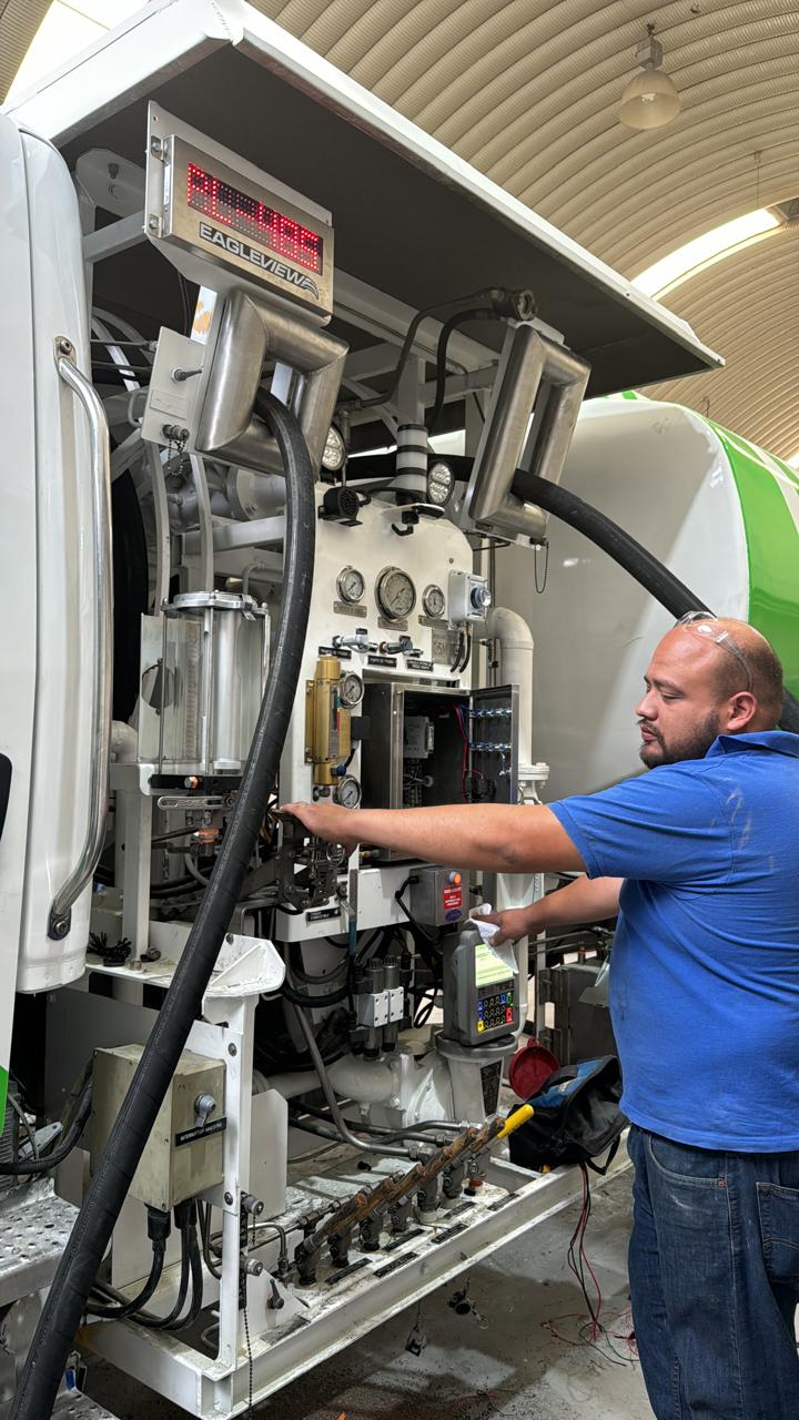 Technician in blue shirt operates machinery on a large vehicle inside a building.