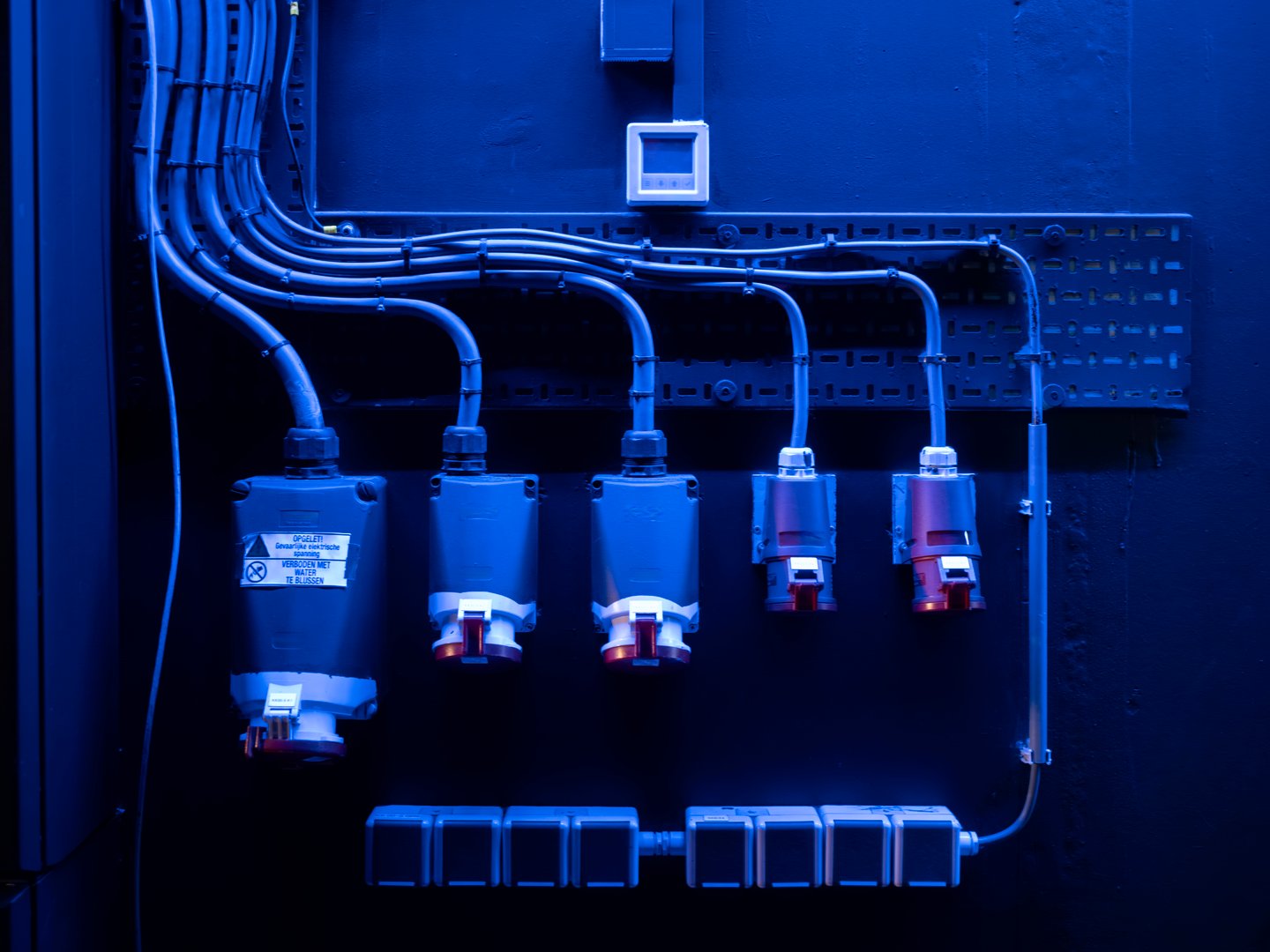 Industrial power sockets and electrical conduit backstage in blue stage lighting, theatre infrastructure
